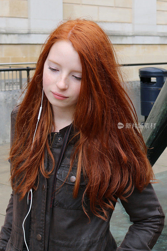 14 / 15岁的红发少女，皮肤苍白，脸上有雀斑，通过耳机听着音乐走在街上，向下看照片